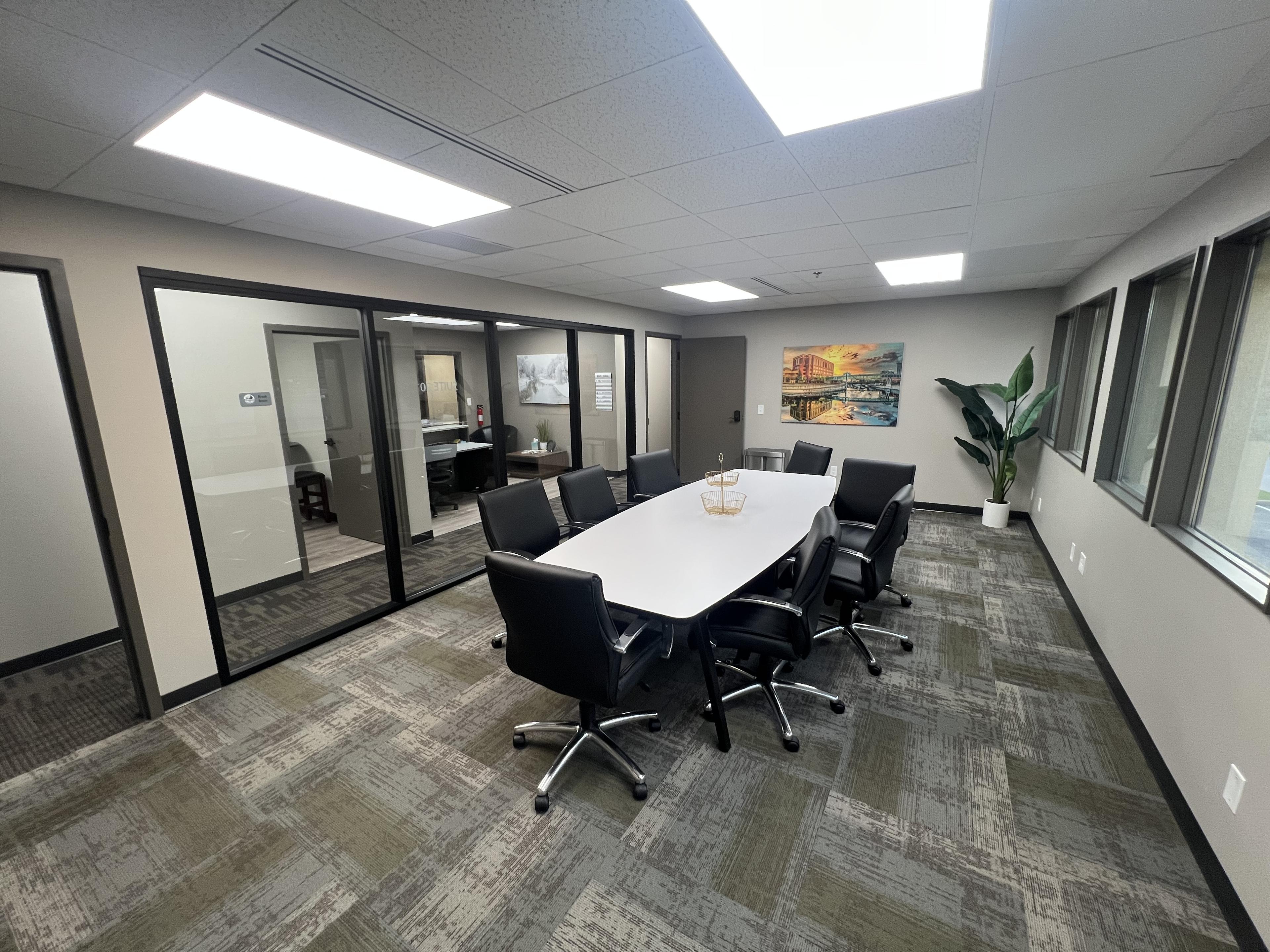 Conference room with white table, eight black office chairs, and a Rochester skyline canvas on the wall